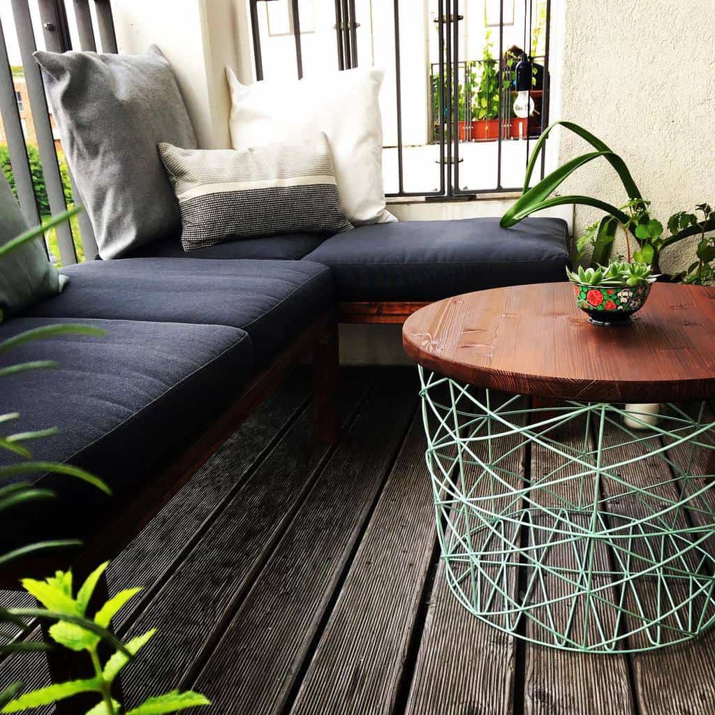 Small cozy balcony with a corner bench, colorful pillows, and a round wireframe coffee table.