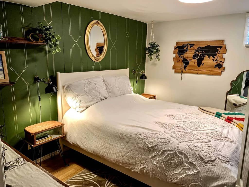 White bedroom with green accent wall, wooden map decor, and round mirror above the bed.
