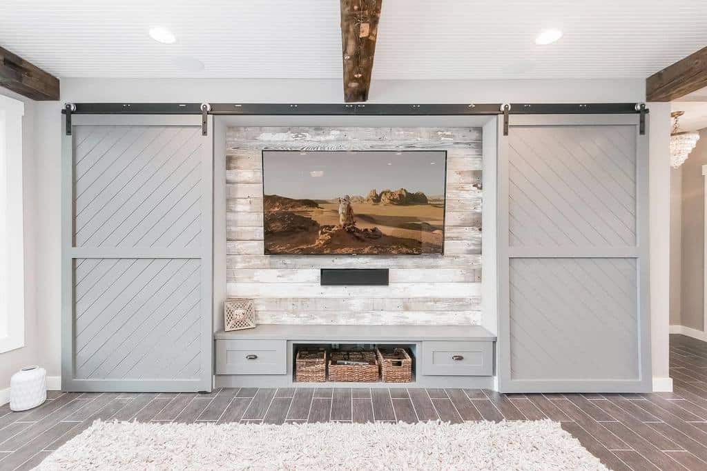 Country-style lounge with gray sliding barn doors, mounted TV, and rustic wooden accent wall.