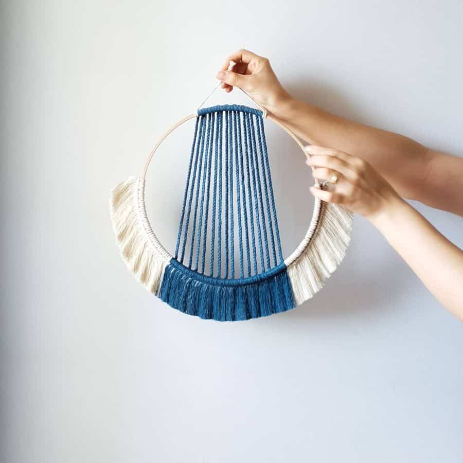 Handcrafted bohemian wall hanging with blue and white yarn on a circular frame.