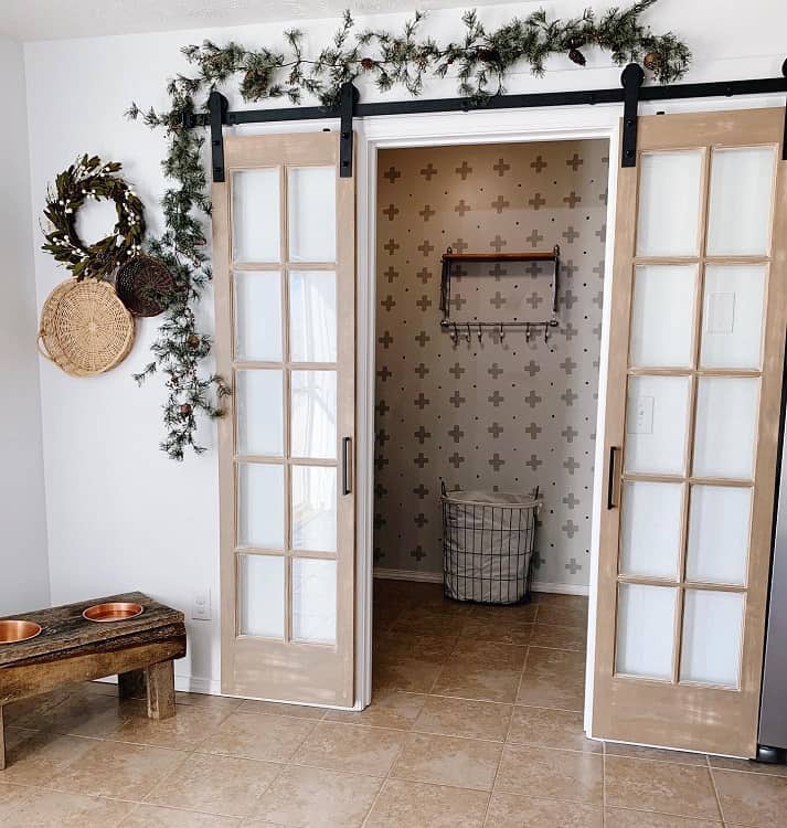 French-style sliding barn doors with glass panes in a rustic entryway decorated with garland greenery above the doors.