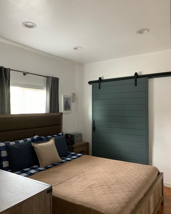 Dark green sliding barn door in a cozy bedroom with a wood-framed bed and plaid bedding.