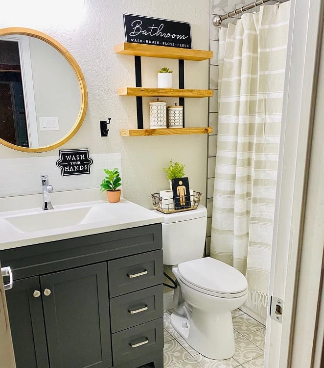 Farmhouse-style bathroom with round mirror, dark vanity, white sink, and wooden shelves decorated with plants