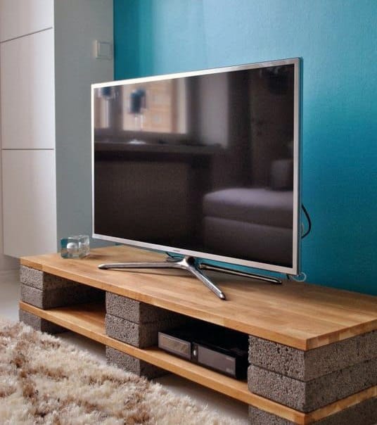 Modern TV on a minimalist stand made of wooden planks and concrete blocks near a blue wall
