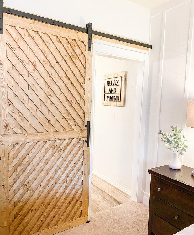 Natural wood sliding barn door with diagonal planks in a cozy master bedroom.