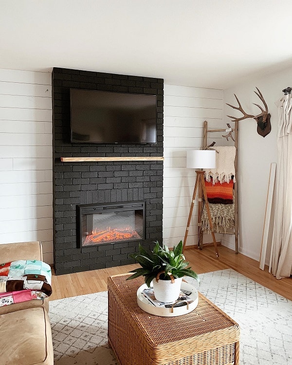 white shiplap wall black brick fireplace surround wall mounted tv wicker chest deer head