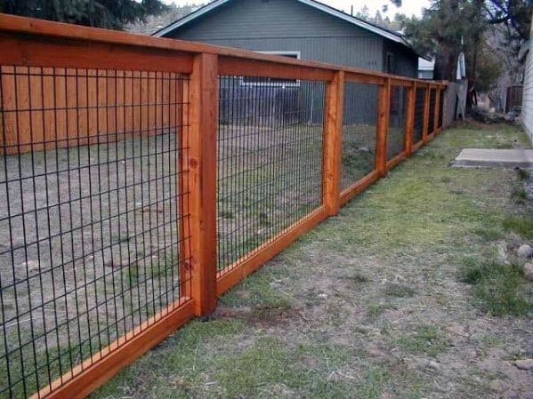 A rustic wooden and wire fence lines the grassy path between two charming houses