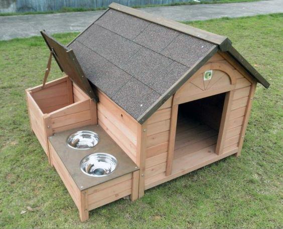Wooden dog house with a sloped roof, two metal food bowls, and a storage compartment on grass