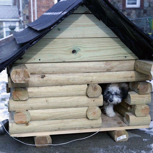 Wooden log cabin-style doghouse with a black roof