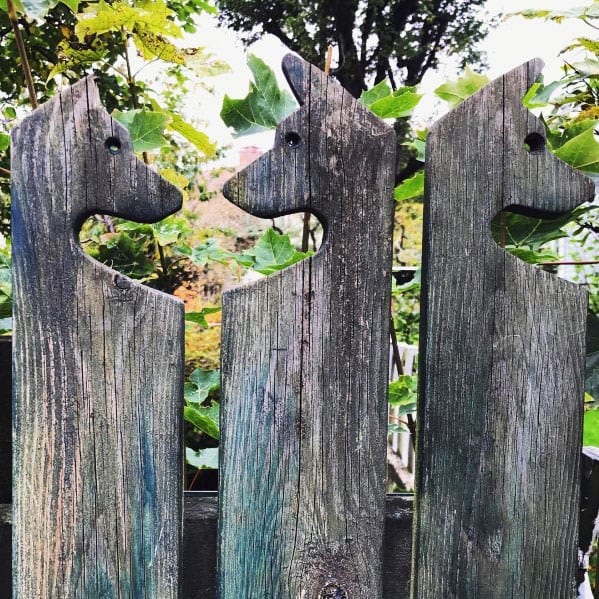 Dog-shaped panels create a charming wooden fence against a lush, leafy backdrop