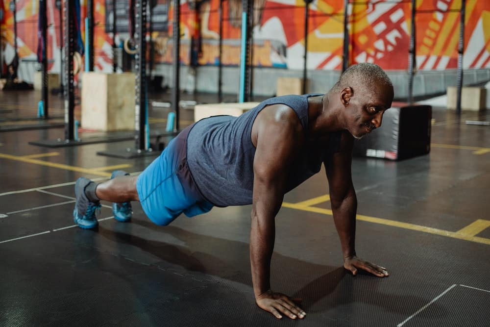 old man in gray tank doing push up on floor in gym