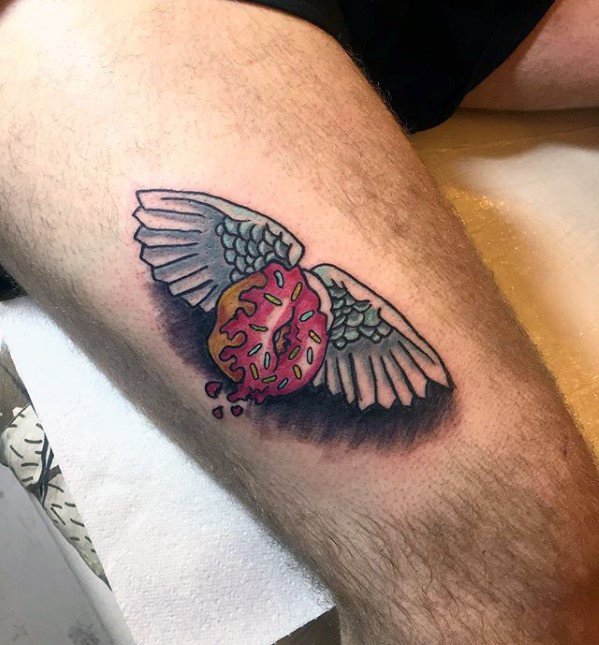 Tattoo of a bitten pink donut with wings and sprinkles, giving a flying or angelic effect with soft shading underneath.