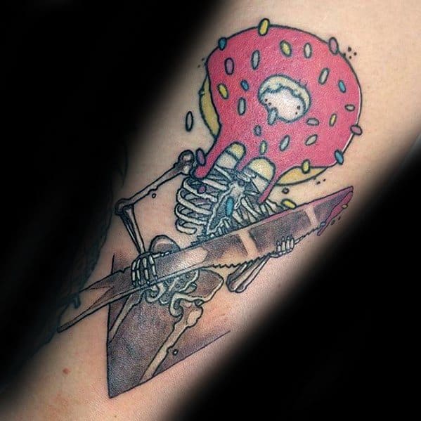 Tattoo of a skeleton holding a scythe with a pink sprinkled donut for a head, blending dark and playful elements in one design.