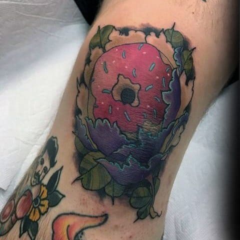 Tattoo of a pink frosted donut wrapped in purple and green cabbage-like leaves, blending food and floral elements creatively.