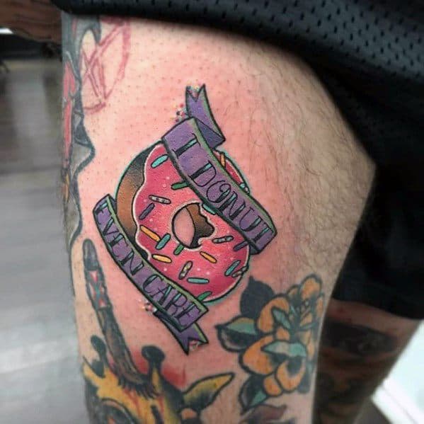 Tattoo of a pink sprinkled donut with a banner that reads I donut even care, combining humor with bold, colorful style.