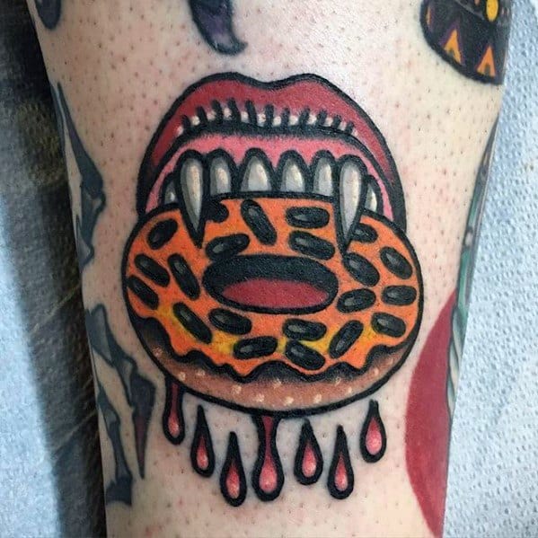 Tattoo of vampire lips with sharp fangs biting an orange chocolate donut, with blood-like drops dripping below for a bold effect.