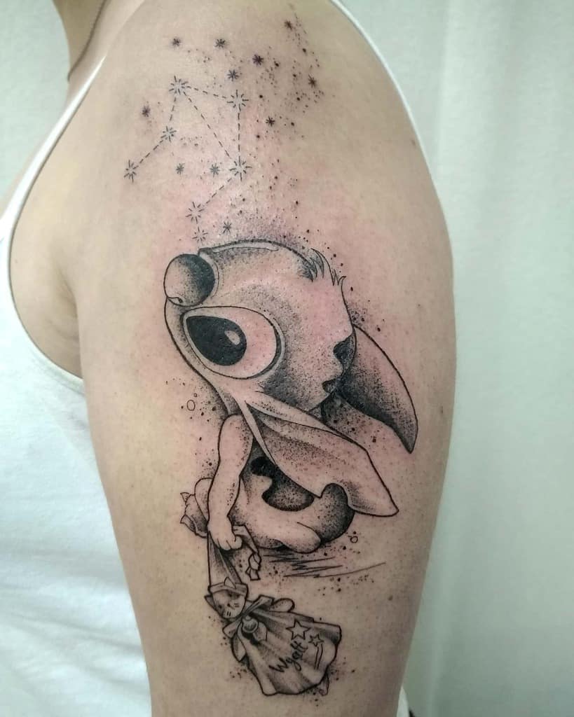 Black and gray tattoo of Stitch from Lilo & Stitch holding a bag with a starry constellation above, placed on the upper arm.