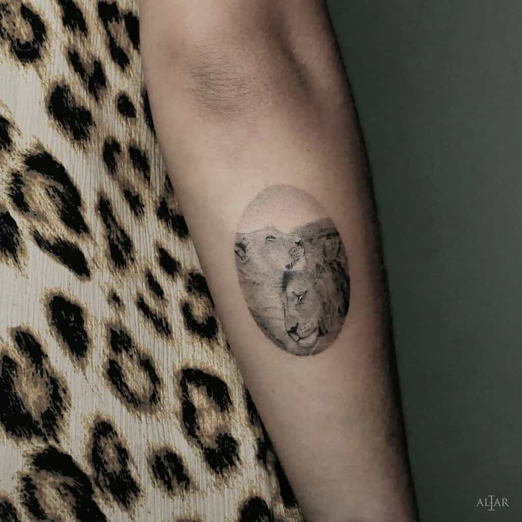 Realistic lioness tattoo on the forearm, featuring a detailed wildlife scene in an oval frame with soft shading and fine black ink.