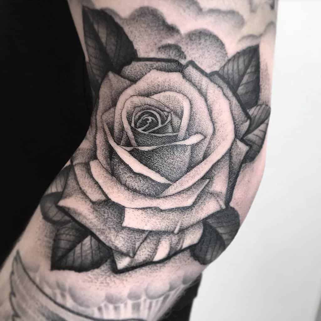Black and gray tattoo of a detailed rose with leaves on an arm