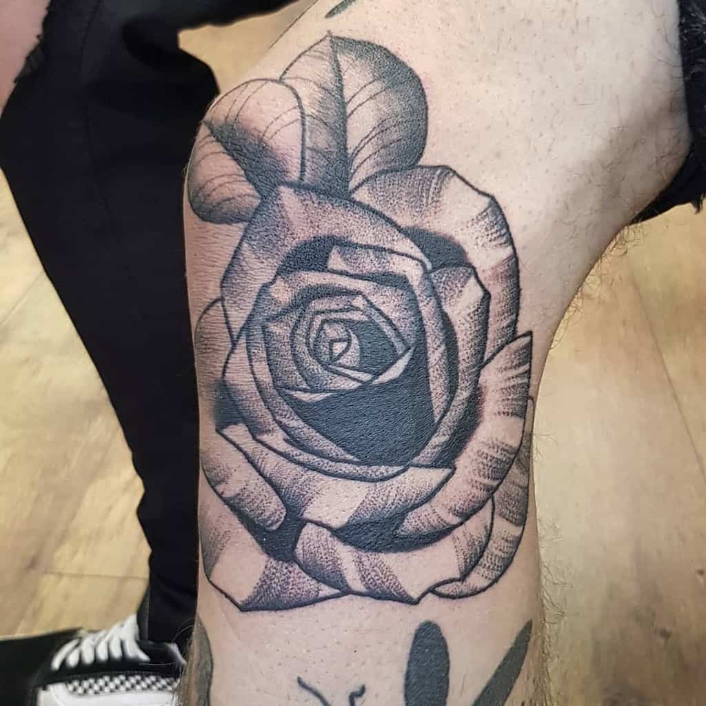 A black and gray tattoo of a detailed rose with dotwork shading, placed on the arm, showcasing intricate lines and depth