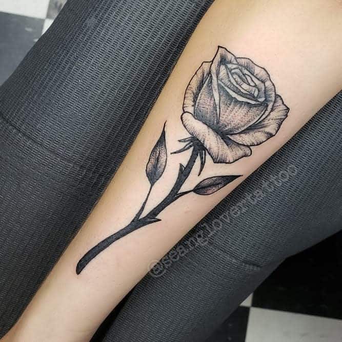 A detailed black and gray rose tattoo beautifully adorns a forearm, seamlessly blending artistry with nature