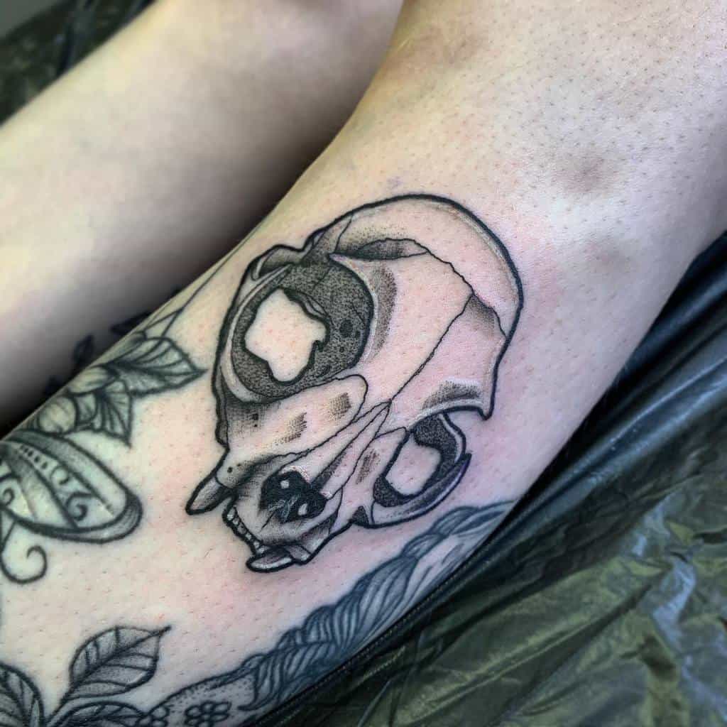 A tattoo of a cat skull on a person's limb, surrounded by various other tattoos