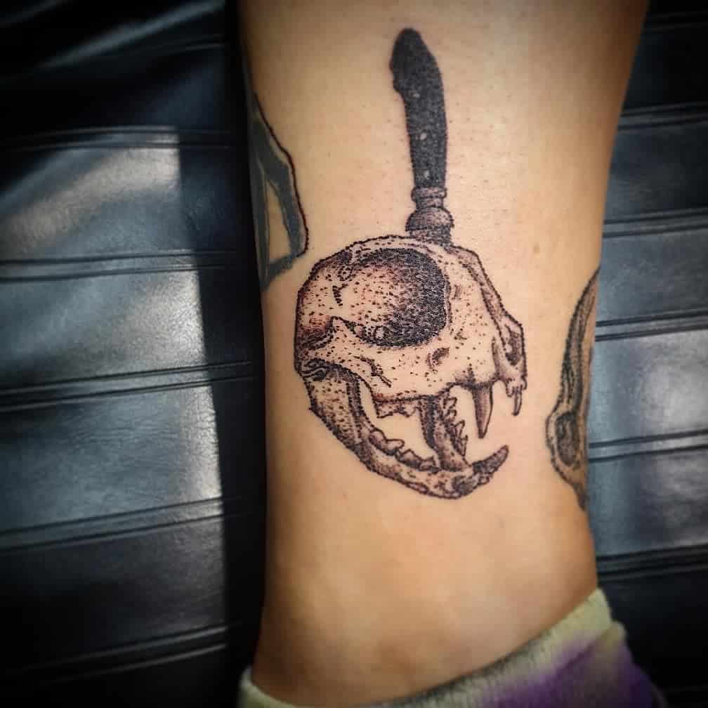 A tattoo of a cat skull pierced by a knife graces the arm