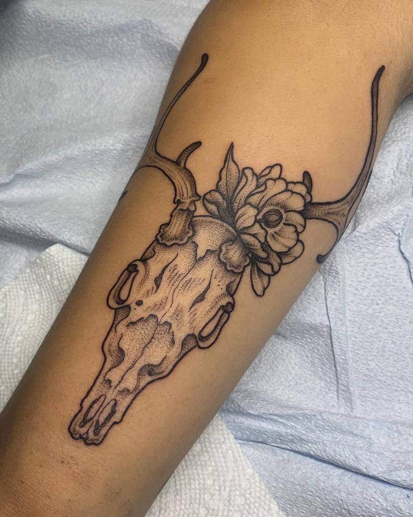 Tattoo of a deer skull with majestic antlers and a flower on an upper arm