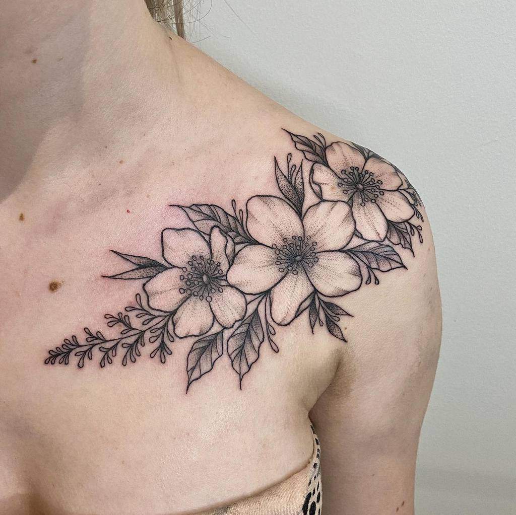 A stunning black floral tattoo on a woman's shoulder, featuring three large flowers with intricately detailed leaves and stems