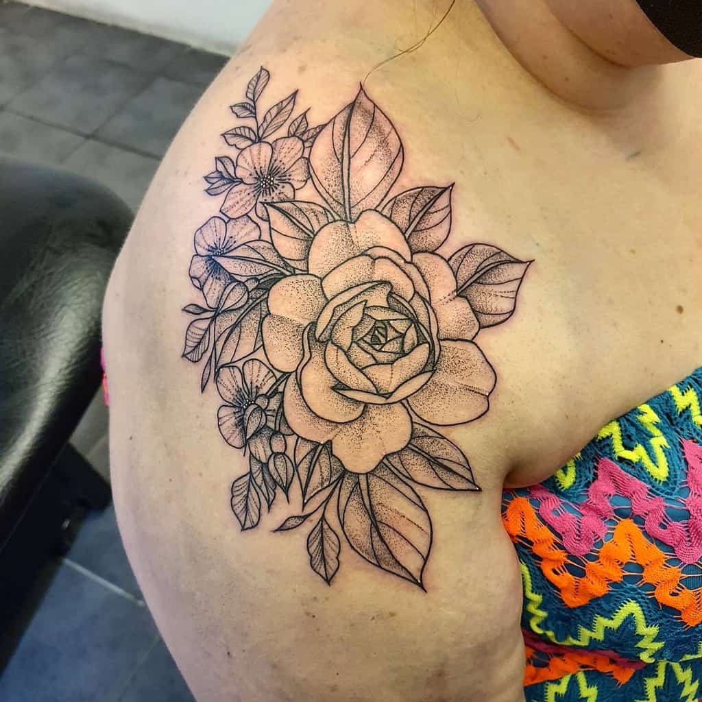 A stunning black-ink floral tattoo with roses and leaves gracefully adorns a woman's shoulder