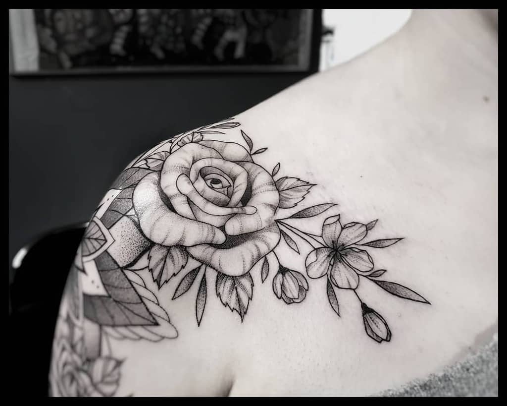 Black and gray tattoo of a rose and flowers on a person's shoulder