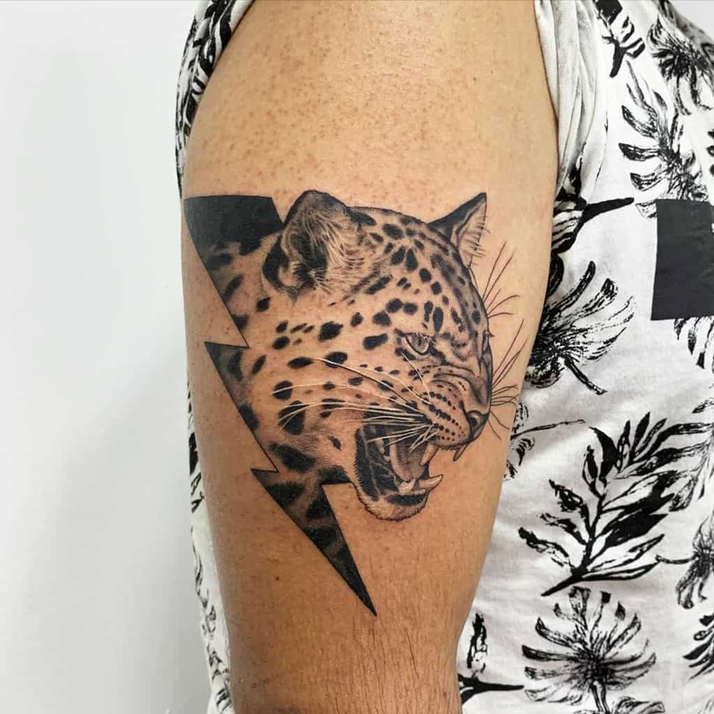 A fierce black and grey tattoo of a jaguar's roaring face, framed by a lightning bolt, wrapping around the upper arm.