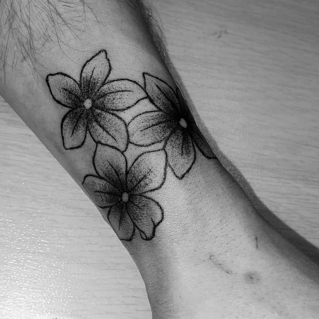 Black and white tattoo of three jasmine flowers on a forearm