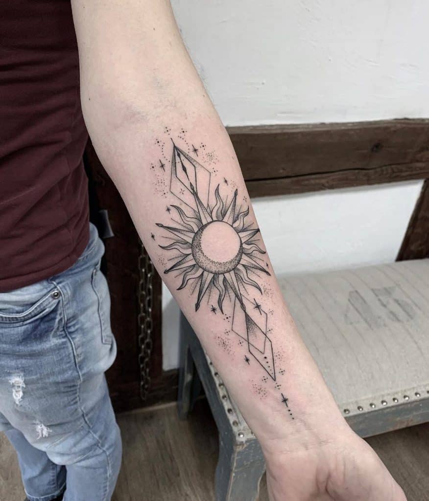 Black ink tattoo of a stylized sun with geometric elements, dot shading, and celestial stars, creating a cosmic and modern forearm design.