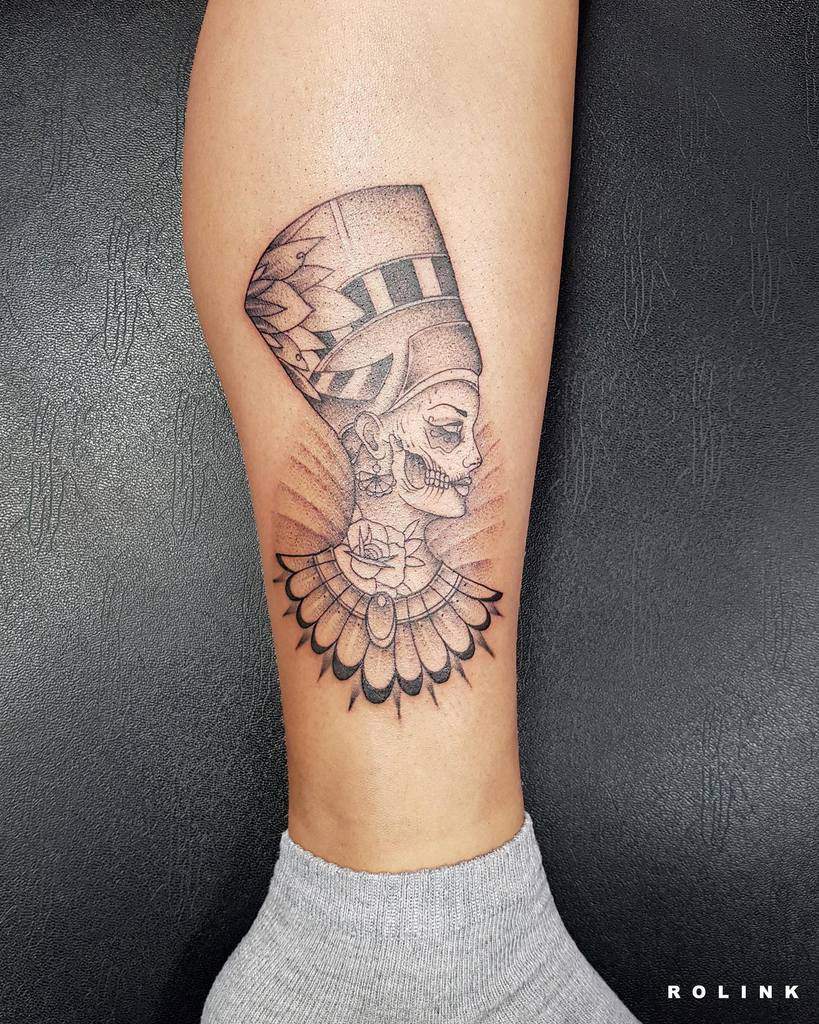 A creative tattoo merging Nefertiti's iconic profile with intricate dotwork and Day of the Dead elements, featuring detailed patterns and shading for a bold and artistic effect
