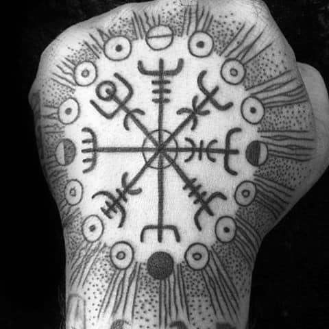 Black and white tattoo of a circular Nordic compass with intricate symbols on a hand