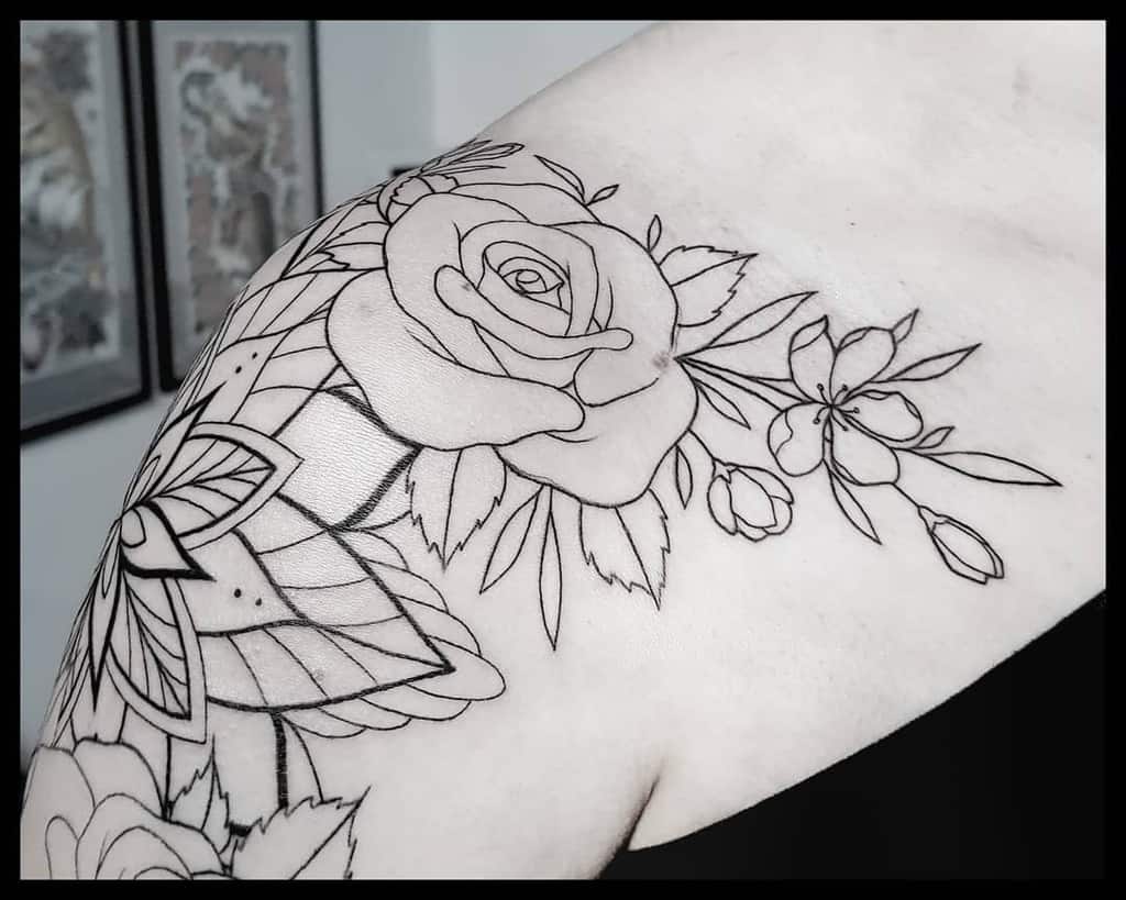Black outlined tattoo of a rose and other flowers gracefully extending from the shoulder to the upper arm