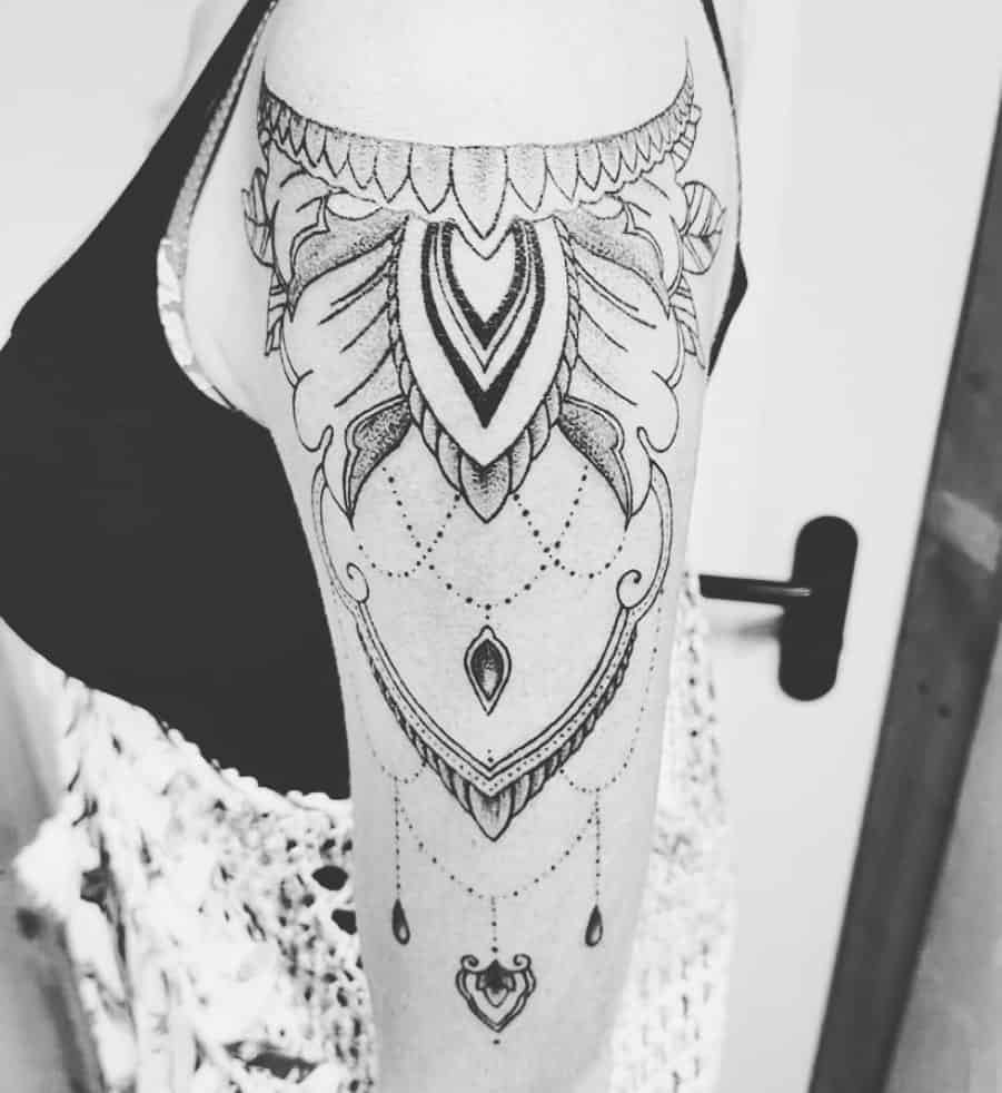 Ornate black ink tattoo on upper arm with detailed geometric and floral patterns, featuring hanging elements