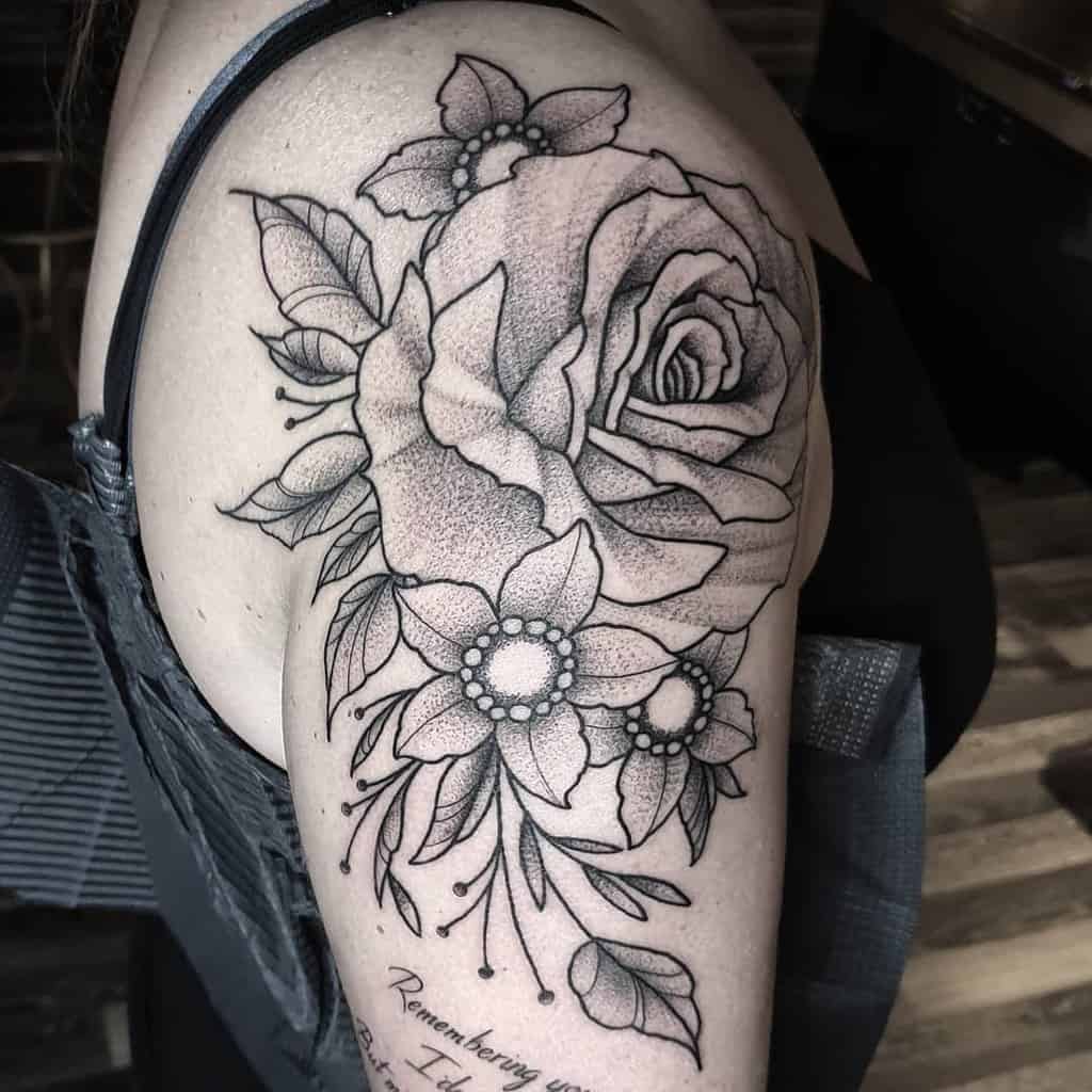 Black and white rose and flower tattoo on upper arm with cursive writing beneath