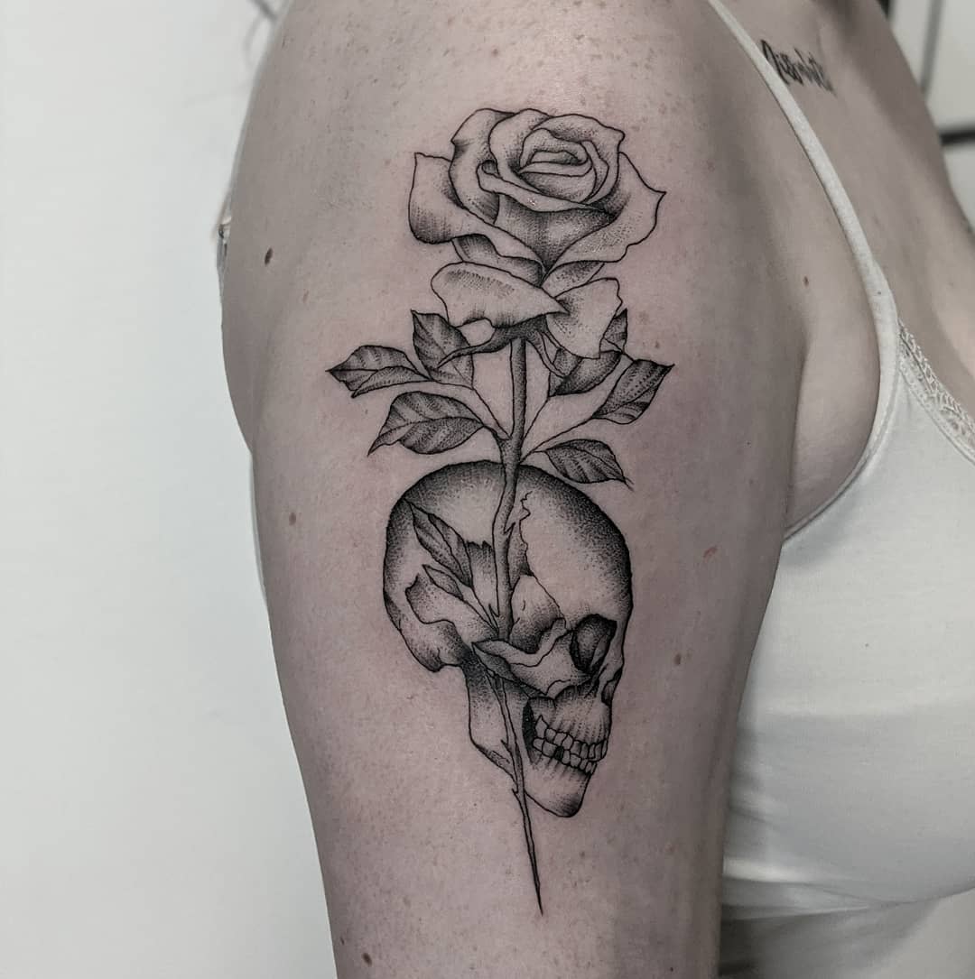 A detailed tattoo on the upper arm featuring a skull with a rose growing through it, blending beauty and mortality in a striking design
