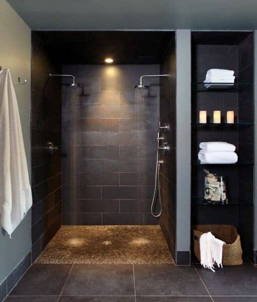 Modern dual shower with dark tiles, recessed lighting, and side shelving for towels and candlelit relaxation