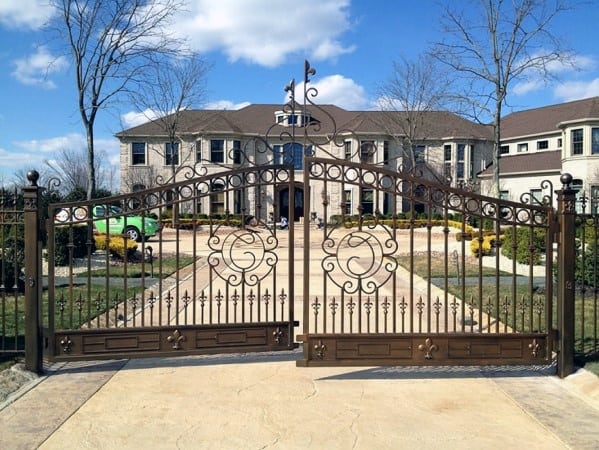 Decorative iron driveway gate with arched design and intricate scrollwork patterns.