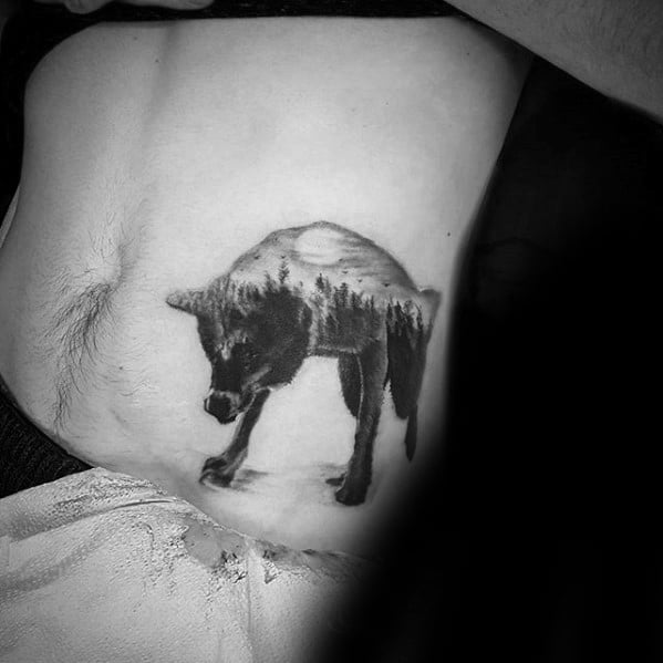 Black and grey tattoo of a wolf with a forest and full moon scene blended into its body, symbolizing wilderness and solitude.