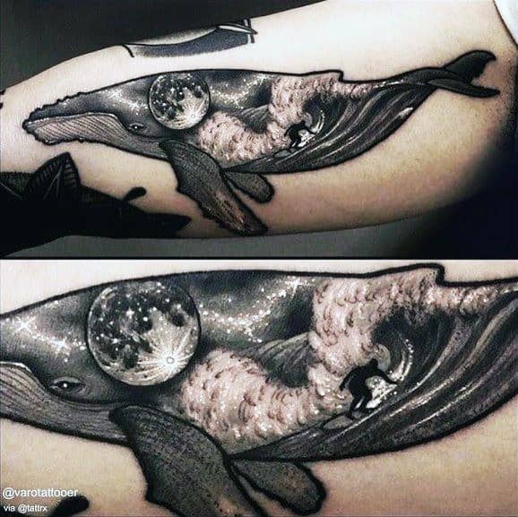 Tattoo of a whale with a moonlit ocean scene inside, featuring waves and a surfer riding through the body of the whale.