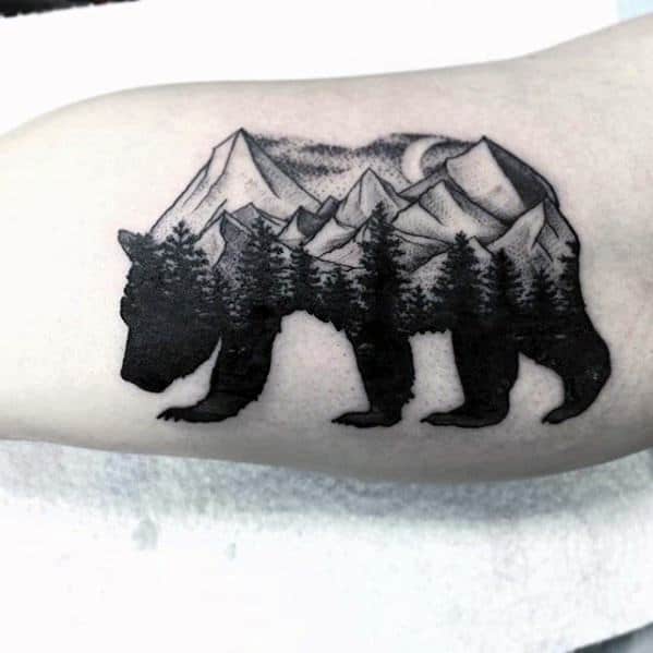 Blackwork tattoo of a bear silhouette filled with pine trees, mountain peaks, and a crescent moon, symbolizing wilderness and strength.