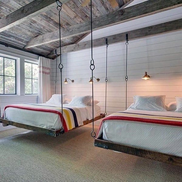 Rustic hanging beds with metal supports, striped bedding, and shiplap walls in a cozy bedroom.