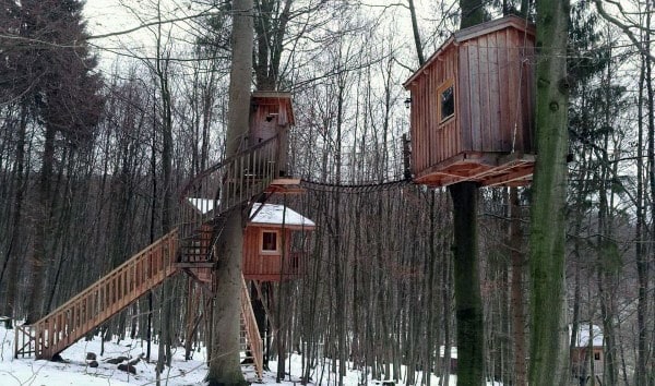 Two wooden treehouses connected by a bridge in a snowy forest
