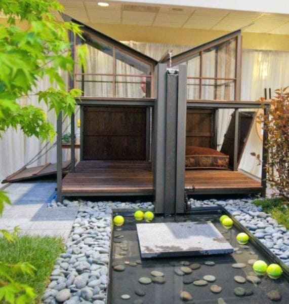 A unique double dog house with modern design, featuring a separated area for each dog, with a stone and water feature surrounded by tennis balls