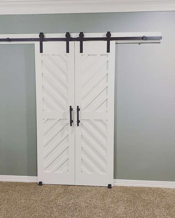 Double white barn doors with diagonal panel design and black hardware against a neutral wall.