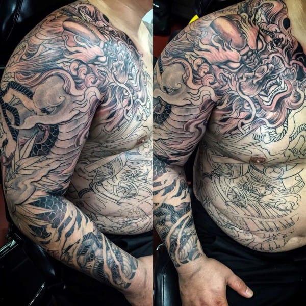 A man with an intricate, large dragon and demon-themed tattoo on his arm and chest